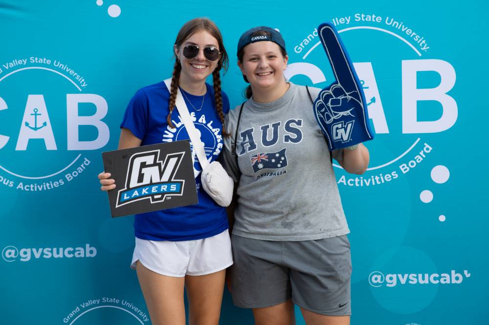 two students posing in front of CAB backdrop at Laker Kickoff photo booth and smiling with a GV sign and foam finger